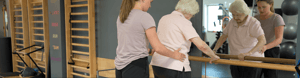 Physical therapist guides her patient holding onto a bar through a balance exercise.