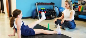 Physical therapist guiding young athlete through leg raise exercise for hip and core rehabilitation.