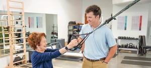 Senior patient performing TRX exercise with physical therapist guidance for orthopedic rehabilitation and functional strength training.