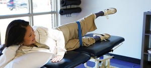 Patient performing a side-lying hip abduction exercise with a resistance band on a treatment table for orthopedic hip and glute strengthening rehabilitation at a physical therapy clinic.