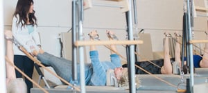 Pilates instructor providing hands-on correction during a small group reformer Pilates class at a clinical Pilates studio.