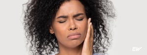 Woman experiencing jaw and facial pain, holding her cheek due to TMJ disorder and temporomandibular joint dysfunction, a common condition treated with physical therapy.