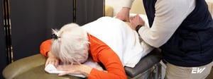 Physical therapist performing manual therapy on older adult patient lying on treatment table.