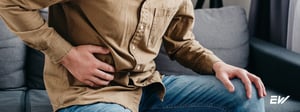 Person seated and holding the lower abdomen, indicating pain associated with a hernia.