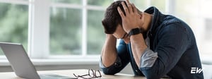 Person experiencing migraine symptoms while seated at a desk, holding head in pain.