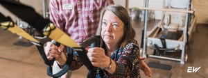 Physical therapist assisting an older adult with suspension-based balance and strength training in a rehabilitation clinic.