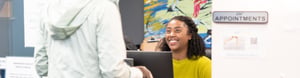 Smiling clinic receptionist greeting a patient at the front desk.