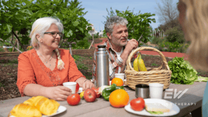 An older couple sits at a picnic table surrounded by fruits and vegetables.