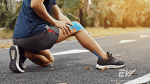 A runner kneels on the road and puts KT tape on their knee.