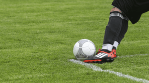A soccer player leans over to make a kick.