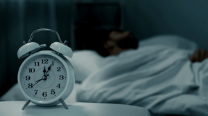 A dark room with an analog alarm clock in the foreground.