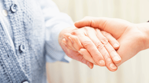 A hand holds the wrinkled hand of an elderly woman.