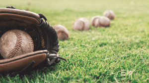 A baseball glove and multiple baseballs lying in the grass.
