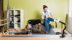 An instructor supervises a woman on a Pilates reformer.