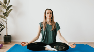 A woman sits in a meditating position on a yoga mat.