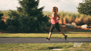 A pregnant woman runs down a sidewalk.