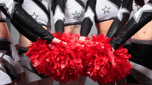 A group of competitive cheerleaders in black & white uniforms hold red pom-poms together in front of them.