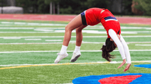 A cheerleader does a back handspring on a football field.