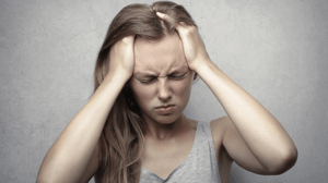 A woman grips her head, visibly in pain.