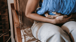 A woman sits in a chair clutching her stomach.