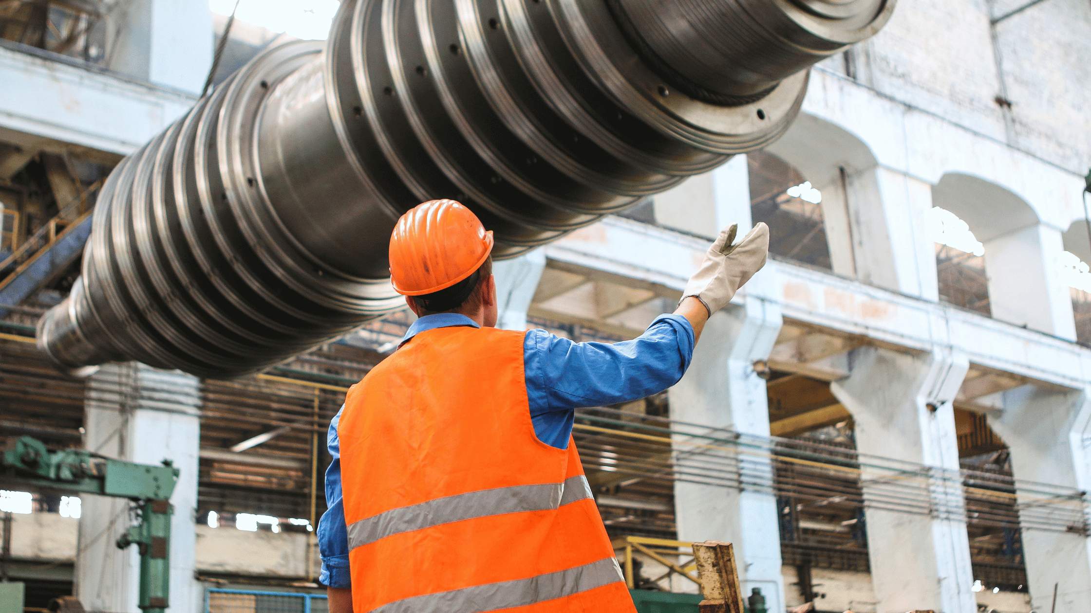 A man in a safety vest and hard hat directs a pipe on a crane.