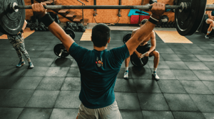 From behind, a man lifts a barbell in a gym.