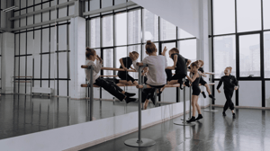 Young dancers play on a barre in front of a mirror.