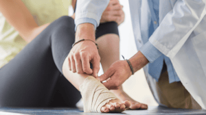 A person sits on an exam table while their ankle is wrapped by a doctor.