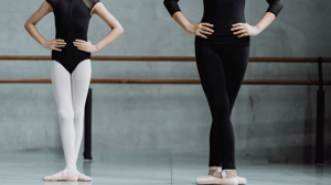 A ballet dancer stands alongside her instructor in second position.