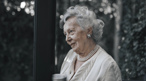 An elderly lady looks out of a window.