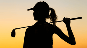 In silhouette, a female golfer holding her club behind her back.