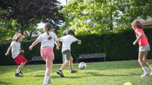 A group of young children kick a soccer ball around outside.
