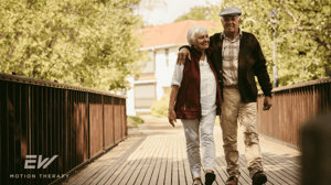 An elderly couple walks outside with their arms around each other.