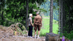 A senior couple stand holding hands in the woods.