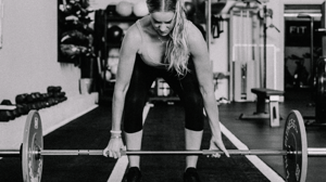 A woman bends down to lift a barbell.
