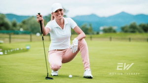 A smiling female golfer squats down on a golf course.
