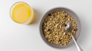 A bowl of bran cereal next to a glass of orange juice