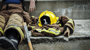 A firefighter sits on a curb with her helmet and jacket beside her.