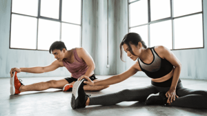 Two people sit on the floor and stretch.
