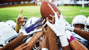 A group of football players all grip the ball from below.