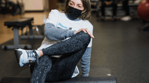 A woman sitting on the floor crosses her leg over her knee.