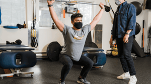 A man squats while holding a golf club over his head.