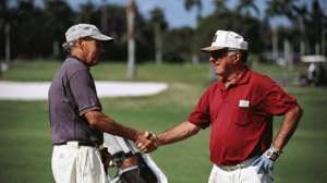 Two older golfers shake hands on the course.