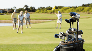 A set of golf clubs in the foreground, with golfers in the background.