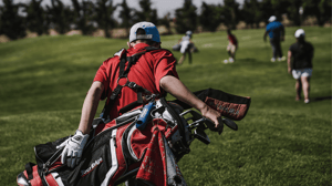 From behind, a male golfer carrying his golf bag.
