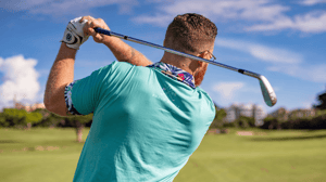 From behind, a golfer takes a swing.