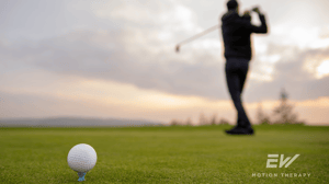 A golf ball in the foreground, with a golfer swinging in the background.