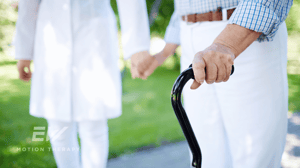 An older couple walks hand in hand, one holding a cane.
