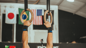 A man's hands grip rings in a gymnastics facility.