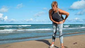 A woman holds her hip in pain standing on the beach.